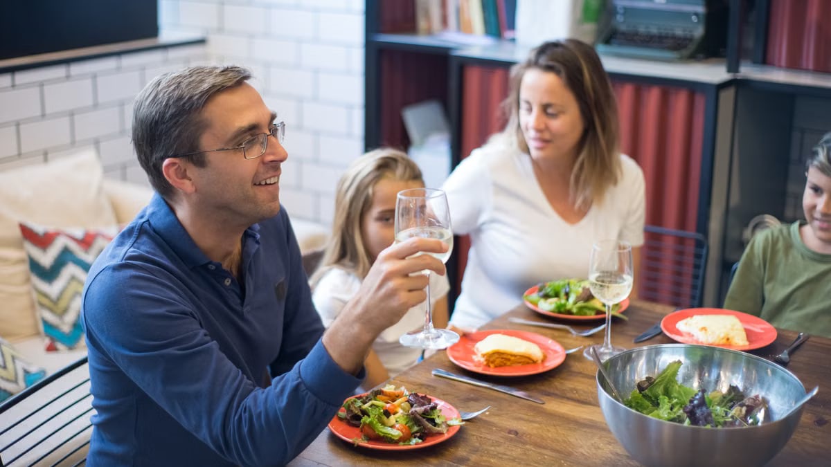 A happy family of four enjoying a meal with salads and wine at home.