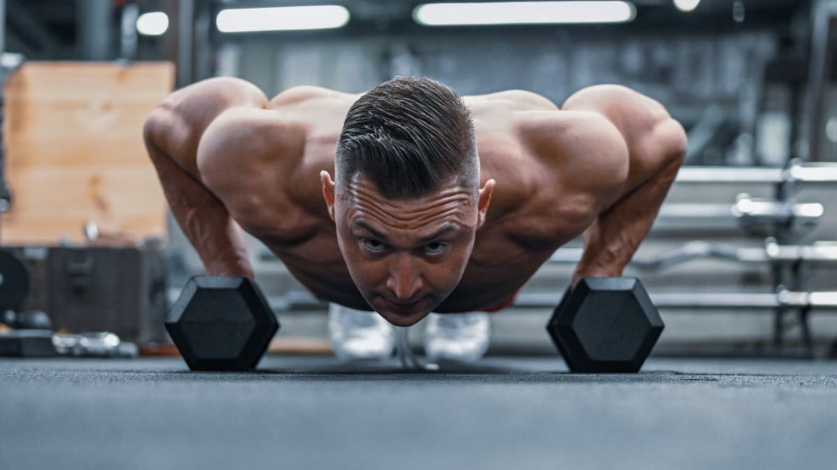 Fit man doing push-ups on hex dumbbells in a modern gym setting.